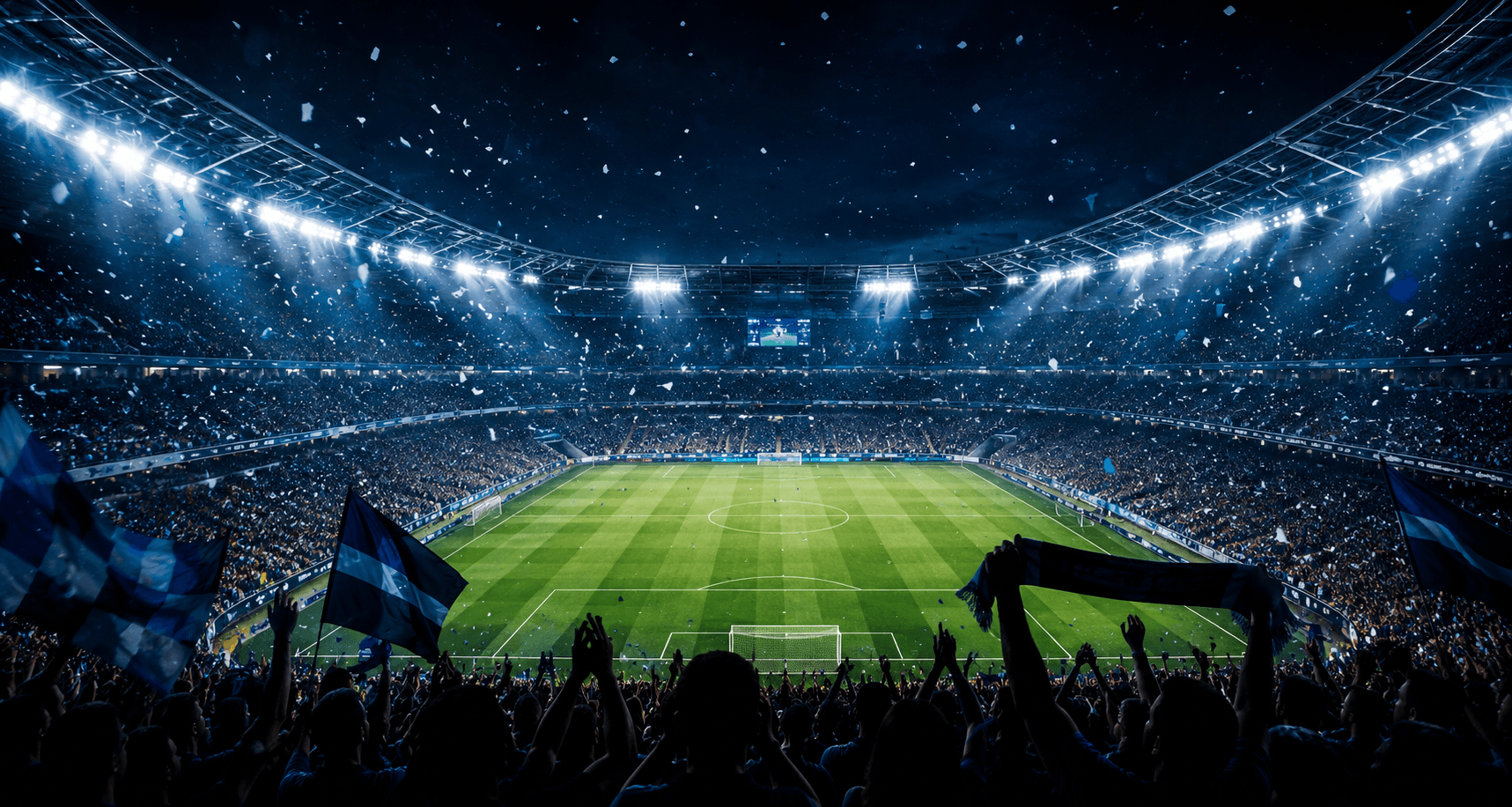 A packed football stadium under the lights with fans waving flags